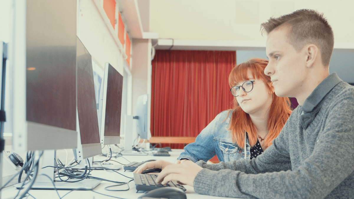 Two students at a desk looking at a computer screen together.